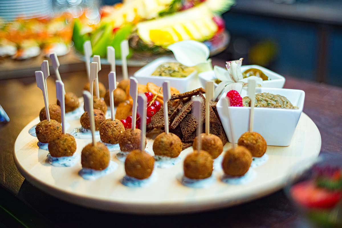 Teller mit Vorspeisen, Catering-Service. Falafelbällchen auf Sahnesauce. Sautierte Aufstriche und Roggenbrösel auf einem runden Holzteller.