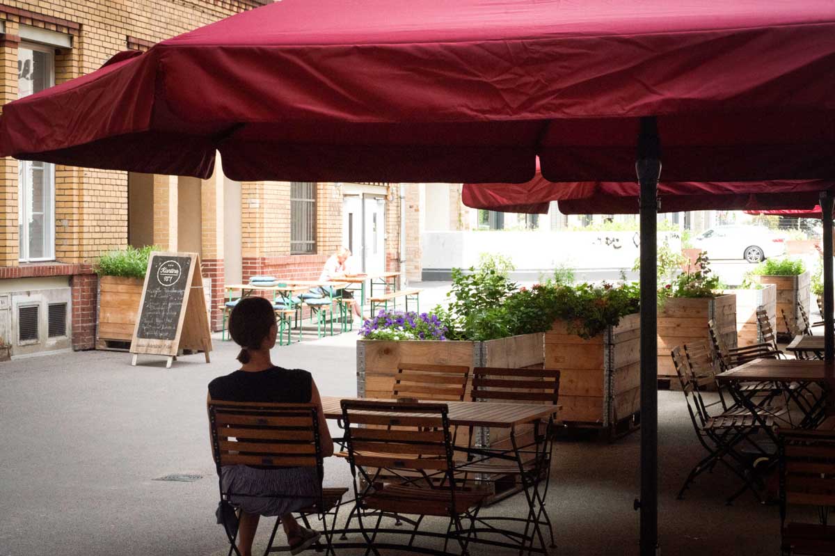 Kantine No 1 draußen sitzt eine Frau auf einem Stuhl unter einem Sonnenschirm in rot